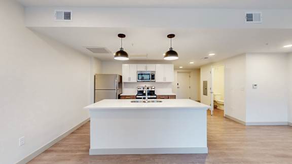 A modern kitchen with a white island and pendant lights.