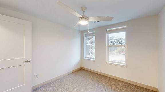 A room with a ceiling fan and two windows.
