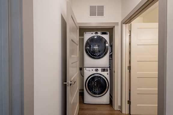 A white washing machine and dryer are stacked on top of each other in a narrow hallway.