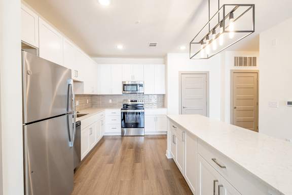 A modern kitchen with a stainless steel refrigerator and wooden floors.