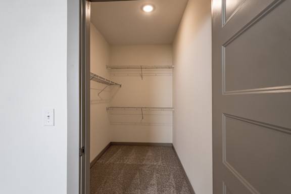 A small, empty room with a door on the left and a closet with a coat rack on the right.