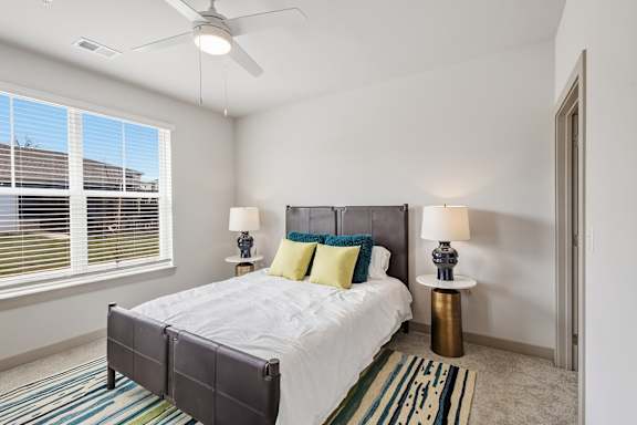 A bedroom with a bed, two lamps, and a ceiling fan.