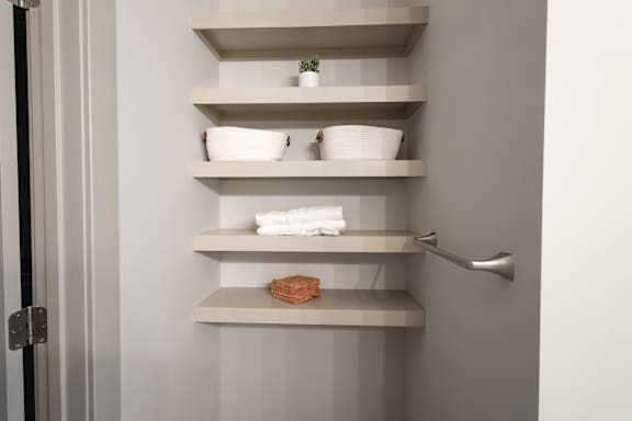 A white shelf with a plant, bowls, and towels.