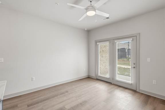 A room with a ceiling fan and sliding glass doors.
