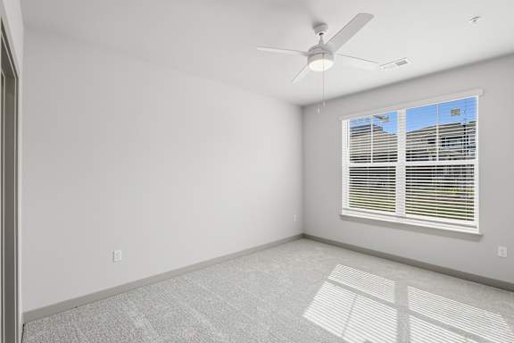 A room with a ceiling fan and a window with blinds.