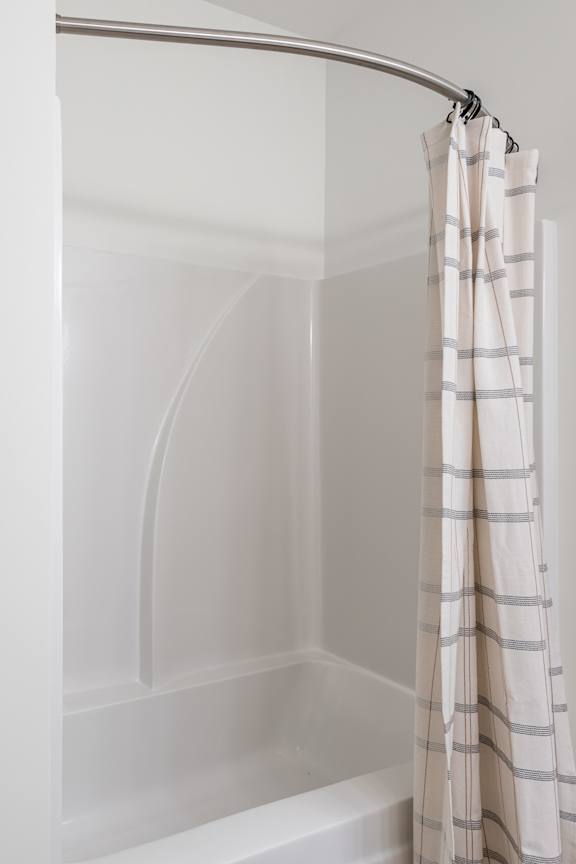 A white shower curtain with grey stripes hangs over a white bathtub at Sage Springs, Elizabethtown, KY