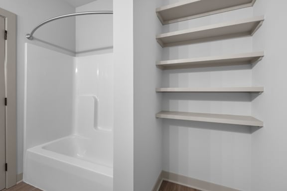 A white bathroom with a tub and shelves.at Forest Edge Apartments, Charlestown, IN 47111