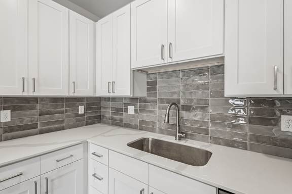 A kitchen with white cabinets and a stone backsplash.