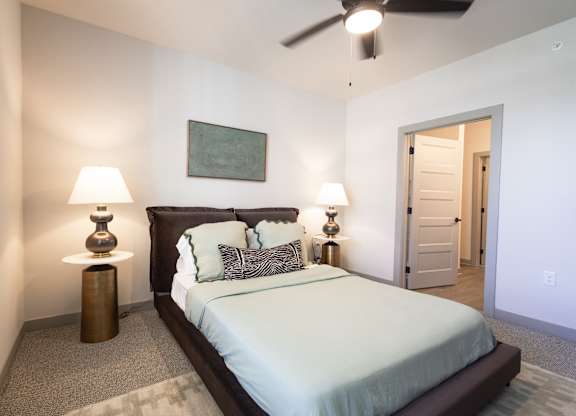 A bedroom with a bed, two lamps, and a ceiling fan.