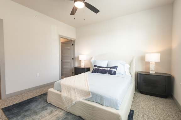 A bedroom with a bed, nightstand, and ceiling fan.