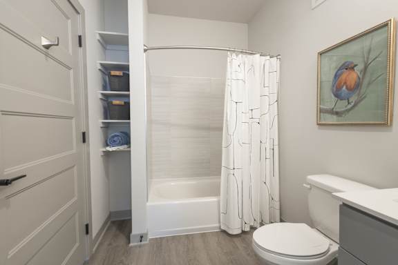 A bathroom with a toilet, a bathtub, a shower curtain, and a painting of a bird.