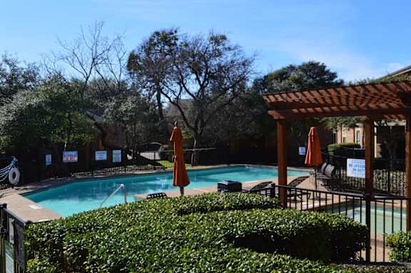 A pool surrounded by greenery and a wooden pergola.