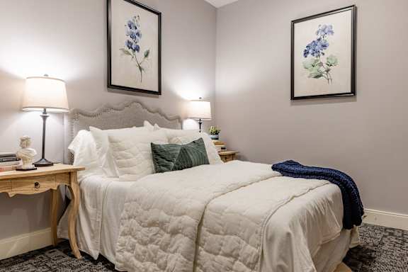 A bedroom with a bed, two lamps, and two framed pictures on the wall.