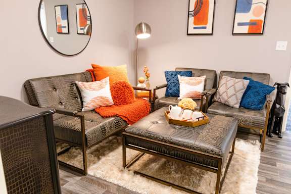 A living room with a grey couch, a brown coffee table, and a round mirror on the wall.