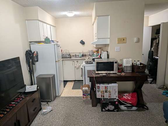 A kitchen area with a refrigerator, microwave, and a table with a computer on it.