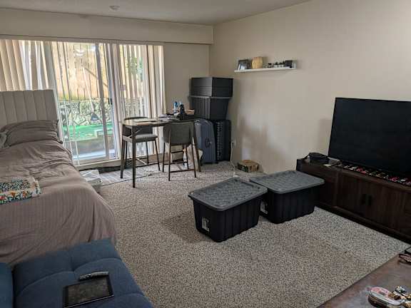 A living room with a couch, a chair, a table, a television, and a window with blinds.