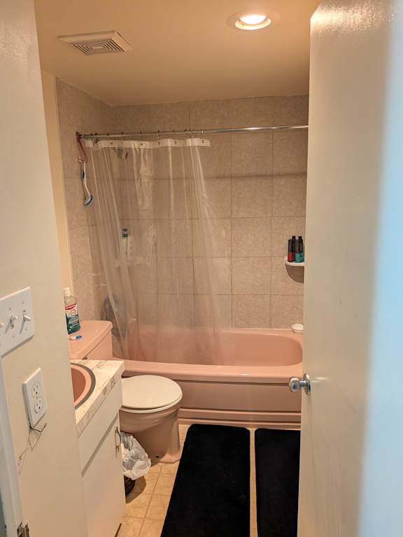 A bathroom with a pink tub, toilet, and sink.
