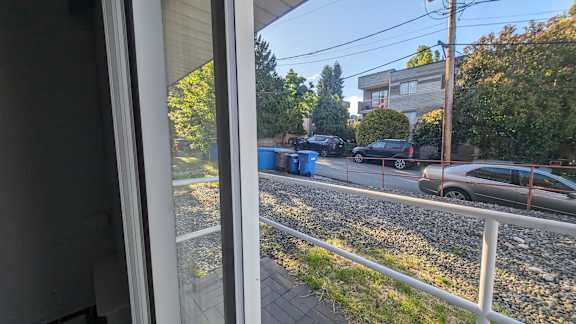 A view from a window looking out to a street with cars and a blue dumpster.