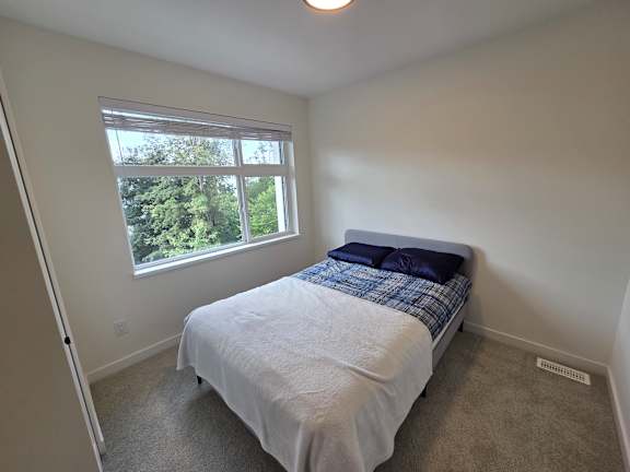 A bedroom with a bed, window, and carpeted floor.