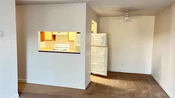A room with a white fridge and a white door leading to another room.