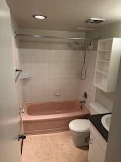 A white bathroom with a pink tub and a white toilet.