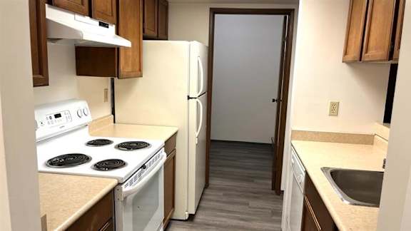 A kitchen with a white stove top oven, white refrigerator, and wooden cabinets.