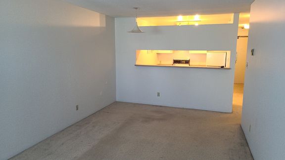 an empty room with a kitchen in the background