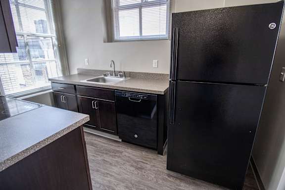 A black refrigerator stands in a kitchen with a sink and cabinets.