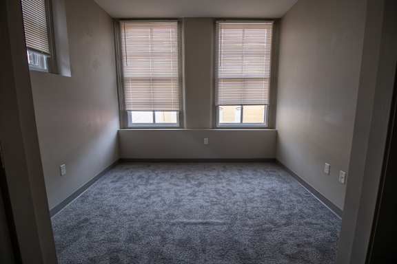 A room with a carpeted floor and two windows.