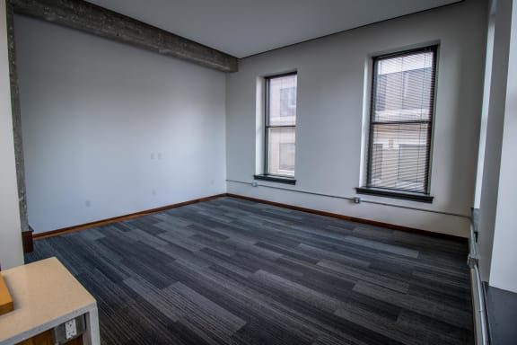an empty room with wood flooring and two windows
