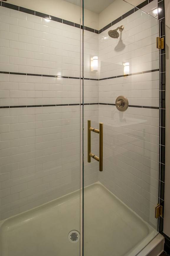 A white tiled shower with a gold handle.