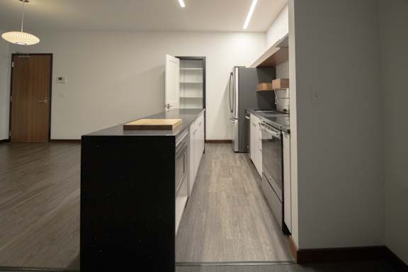 an empty kitchen with white walls and wooden floors and a refrigerator