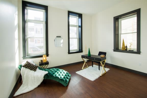 a living room with a couch and a desk and three windows