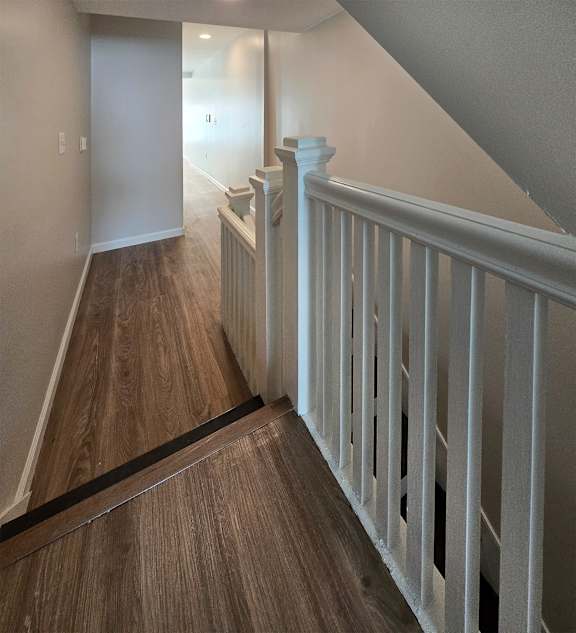 A hallway with a white railing and wooden floors.