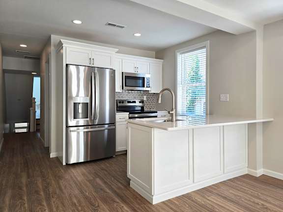A modern kitchen with a stainless steel refrigerator and white cabinets.