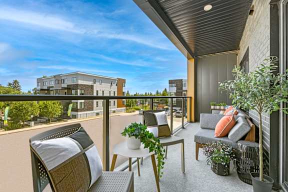 A balcony with a table, chairs, and potted plants overlooks a building.
