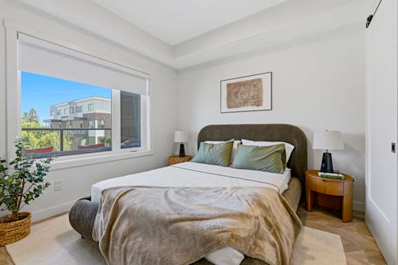 A bedroom with a large bed and a view of a building outside the window.