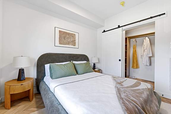 A bedroom with a bed, a nightstand with a lamp, and a closet with clothes.