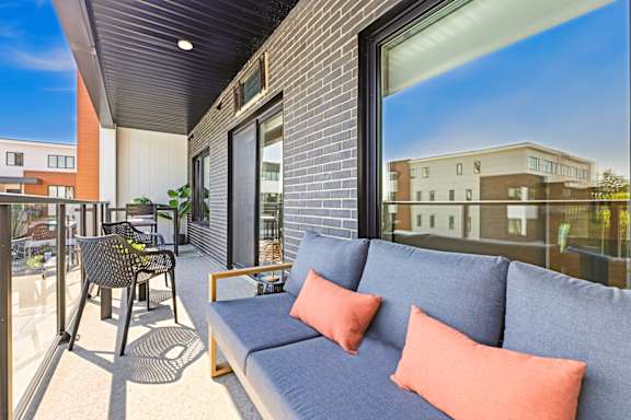 A balcony with a grey couch and orange pillows.