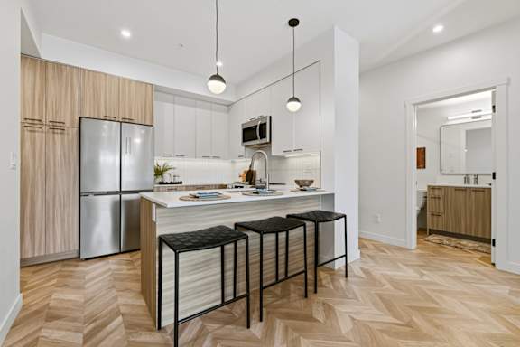 A kitchen with a refrigerator, stove, and bar stools.