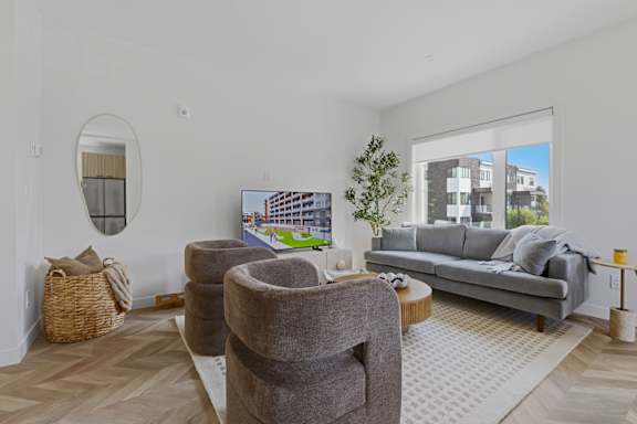 A living room with a grey couch, a round mirror, and a coffee table.