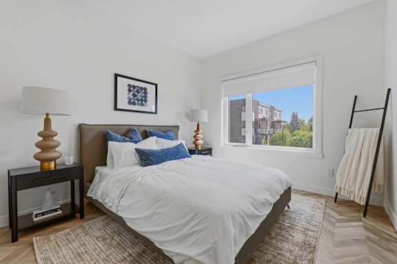 A bedroom with a large bed and a view of a building outside the window.