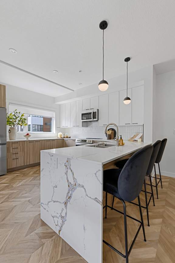 A modern kitchen with a marble island and black chairs.