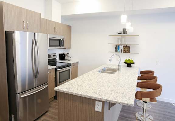 A kitchen with a refrigerator, microwave, oven, sink and bar stools.