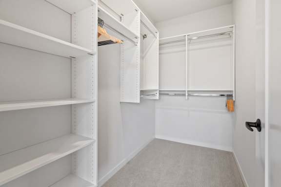 a walk in closet with white shelves and a white closet door