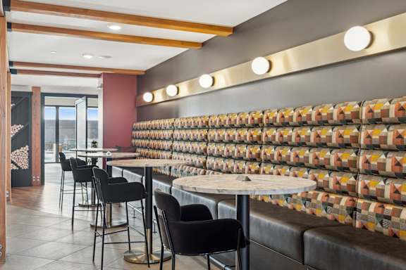 A restaurant with a long table and chairs with a wall of tiles behind it.