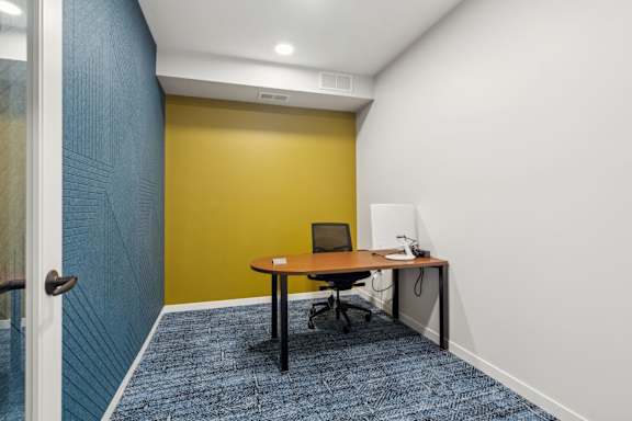 A room with a yellow wall and a desk with a laptop on it.
