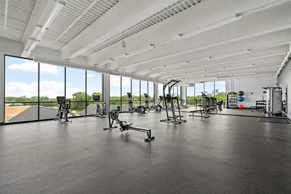 A spacious gym with a variety of equipment and a view of the outdoors through large windows.
