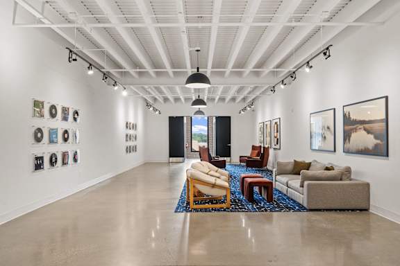 A spacious art gallery with a variety of artwork displayed on the walls and a seating area with a couch, chairs, and a coffee table.