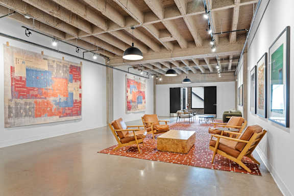 A room with a large painting on the wall and a few chairs and tables.